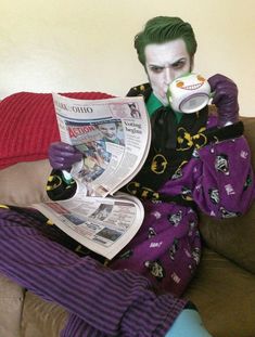 a man with green hair is sitting on a couch drinking from a cup and reading a newspaper