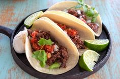 three tacos on a plate with lime wedges