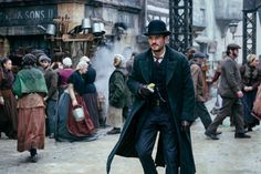 a man in a top hat and trench coat walking down a street with other people