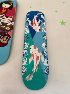 two skateboards with designs on them sitting next to each other, one has a koi fish design on it