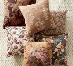 pillows are arranged on the bed with different patterns and colors, including pinks, oranges, yellows, and browns