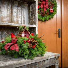 a christmas wreath sitting on top of a wooden bench next to a door with pine cones and red berries