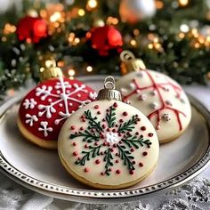 three decorated cookies sitting on top of a white plate next to a christmas tree with red and green decorations