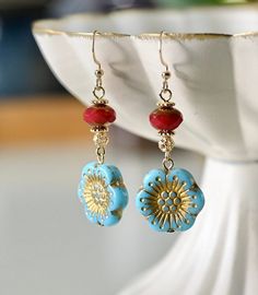 a pair of blue and red earrings sitting on top of a white plate next to a bowl