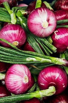 red onions are piled on top of each other with green stems in the foreground