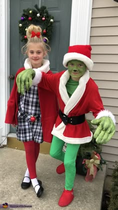 two children dressed up as grin and mrs claus for christmas outside their home in front of the door