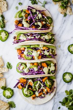 four tortillas filled with veggies and sauce on top of a marble counter