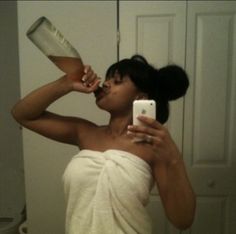 a woman taking a selfie with her cell phone and drinking from a glass in the bathroom