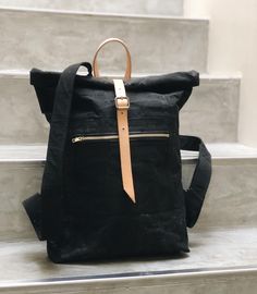 a black backpack sitting on top of a set of stairs with a tan leather strap