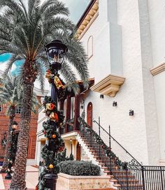 a street light with christmas decorations on it in front of a white building and palm trees