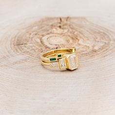 two gold rings with green and white stones on top of a tree stump in the woods