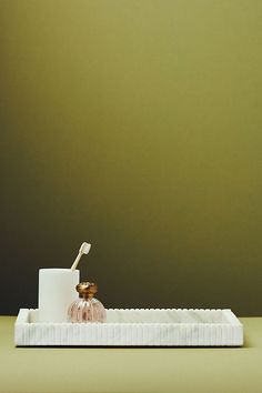 a toothbrush holder sitting on top of a white tray next to a green wall