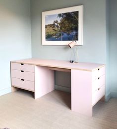 a pink desk with two drawers and a painting on the wall in an empty room