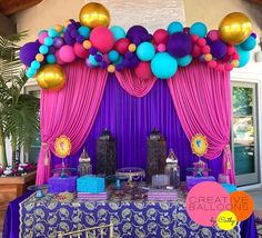 a table topped with lots of balloons next to a purple drape covered stage set up