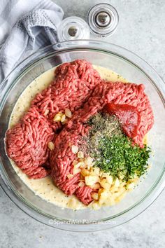 the ingredients for meatballs are in a glass bowl on top of a marble counter