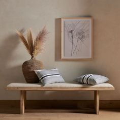 a wooden bench with two pillows and a vase on it in front of a wall