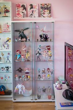 there are many anime figurines on display in the glass case behind the television