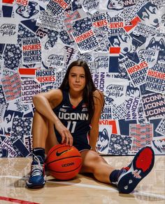 a woman sitting on the floor with a basketball in front of a wall full of stickers