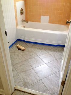 a bathroom with tile flooring and a bathtub in the corner, next to a door