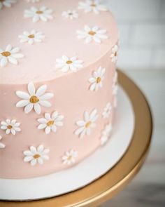 a pink cake with white daisies on it sitting on a gold plated stand