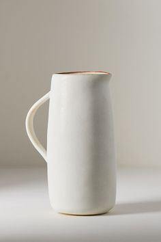 a white coffee mug with a wooden handle on a plain tableclothed surface in front of a gray background