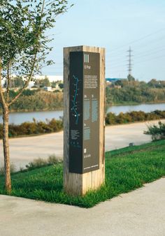 a wooden sign sitting on top of a lush green field next to a tree and water