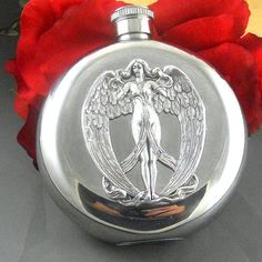 a silver flask with an angel design on it and red flowers in the background