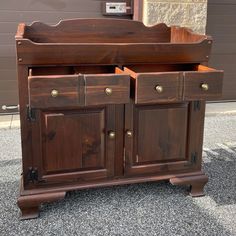 a wooden cabinet with two doors and drawers on the bottom half of it, sitting in front of a garage door