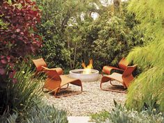 an outdoor fire pit surrounded by plants and chairs in the middle of a gravel area