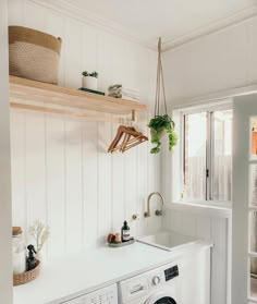 a washer and dryer in a white laundry room with plants hanging from the ceiling