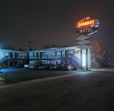 the exterior of a motel at night with cars parked in front and on the street