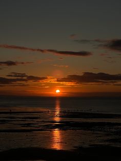 the sun is setting over the ocean with surfers