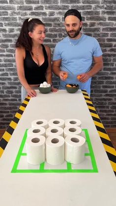 a man and woman standing next to a table with rolls of toilet paper on it