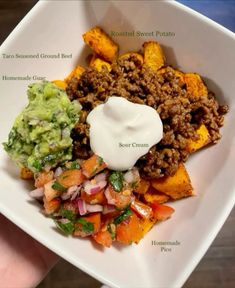 a white bowl filled with taco salad and sweet potato wedges, topped with sour cream