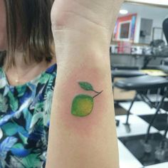 a small tattoo on the wrist of a woman's arm with a green apple