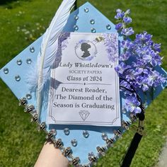 a blue graduation cap with purple flowers and a feather quill attached to it, sitting in the grass