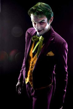 a man dressed as the joker in a dark suit and yellow tie with his hands on his hips