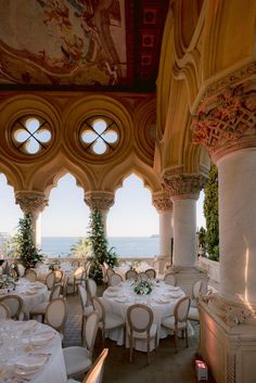 an ornately decorated dining room with white tables and chairs, overlooking the ocean on a sunny day