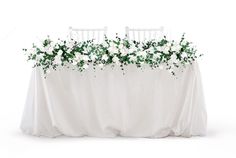 the table is covered with white flowers and greenery as well as two chairs at the end