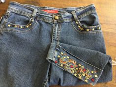 a pair of jeans with beading on them sitting on top of a wooden floor