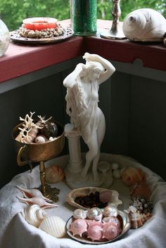 a window sill filled with shells and other items next to a statue on a table