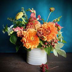 a white vase filled with lots of flowers on top of a wooden table next to a blue wall