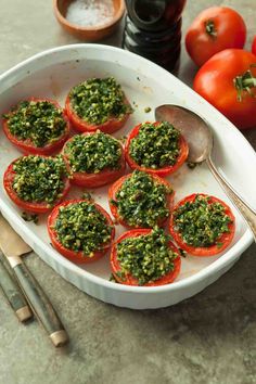 tomatoes with pesto on top in a white dish next to spoons and spices