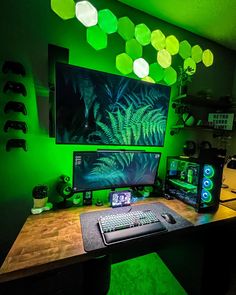 a computer desk with two monitors and keyboard on top of it in front of a green wall