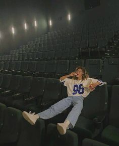 a woman is jumping in the air with her legs spread out while wearing jeans and a football jersey