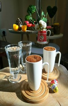 two mugs filled with hot chocolate on top of a wooden table next to glasses