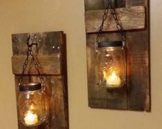 two mason jars are hanging on the wall with candles in them as if they were made from wood planks