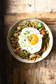 a bowl filled with noodles, meat and an egg in it on top of a wooden table