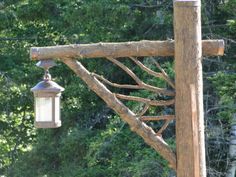 an old fashioned light hanging from a wooden post in front of some trees and bushes