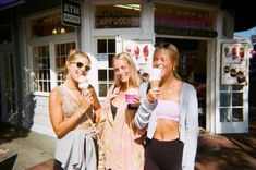 three young women standing in front of a store holding ice cream cones